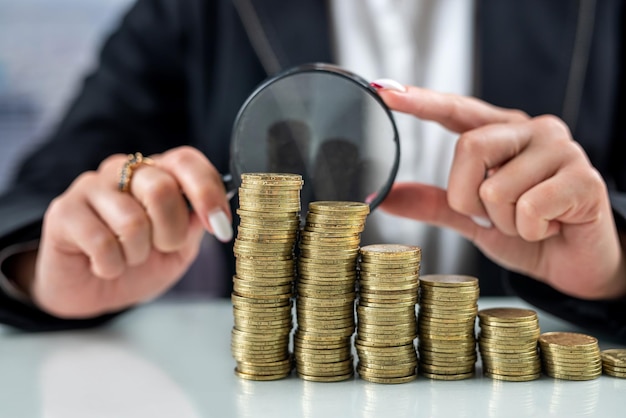 Hand with magnifying glass and money coins stack on office desk