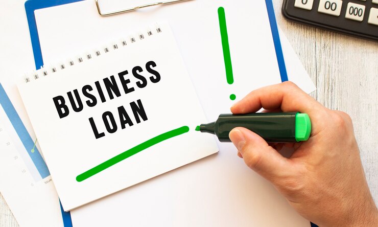 マーカーの付いた手は、デスクトップ上のノートにBUSINESSLOANというテキストを書き込みます。上からの眺め。