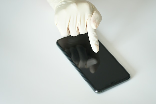 セレクティブフォーカスでスマートフォンに触れる医療用手袋の手