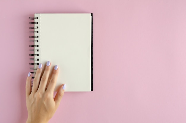 Hand with note pad composition on pink background.