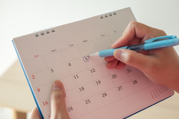 Hand with pen mark at 5th on calendar date with blue\
circle