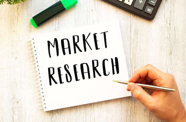 펜으로 손이 나무 책상에 노트북에 MARKET RESEARCH 텍스트를 씁니다.