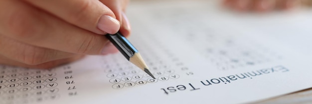 Hand with pencil on examination test paper close up education study school and university