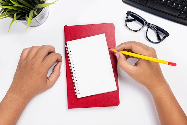 Hand with pencil writing in note book on white desk