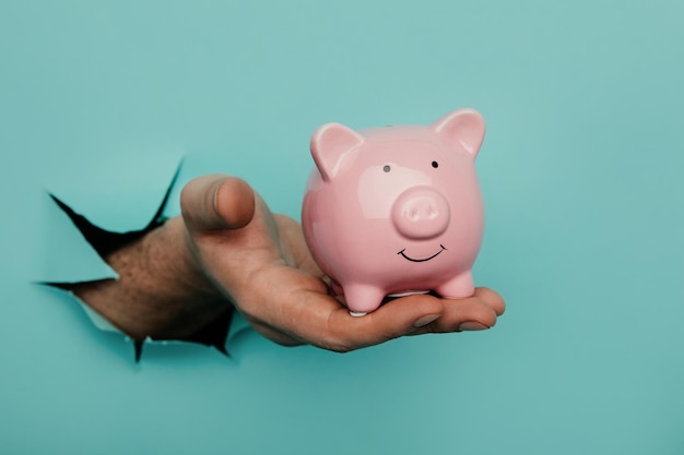 Photo hand with a pink piggy bank through a blue paper hole financial and business concept