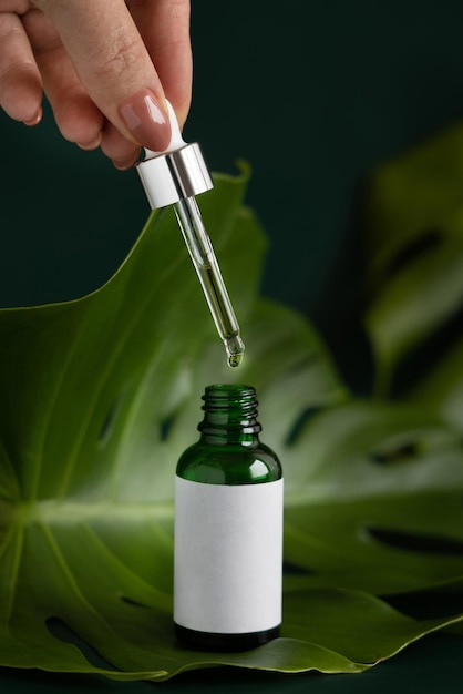 Hand with a pipetta of Bottle on monstera leaf on green table close up Mckup