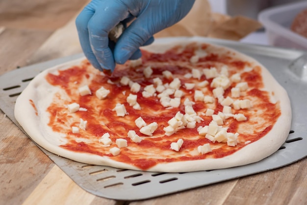Photo hand with plastic glove preparing pizza with tomato sauce and fresh mozzarella on a shovel on a wooden board close up