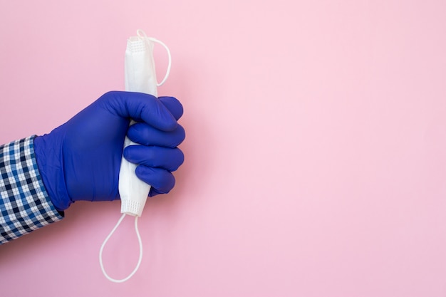 Hand with protective mask in medical gloves isolated on pink background. Mask for covering the mouth and nose. The concept of protection against bacteria and viruses.