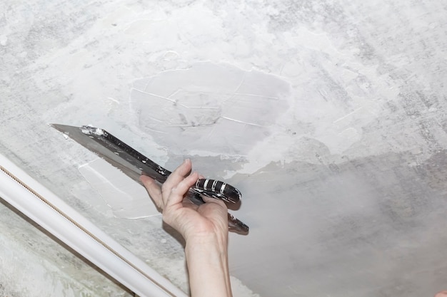 Hand with a putty knife and putty apply mastic to the ceiling to level the surface