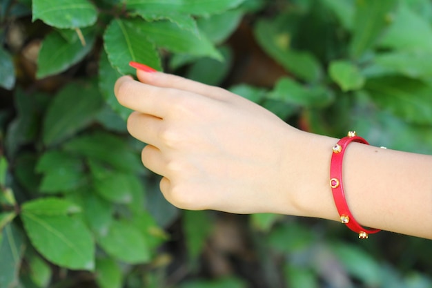 A hand with a red bracelet and red bracelets holds a green leaf.
