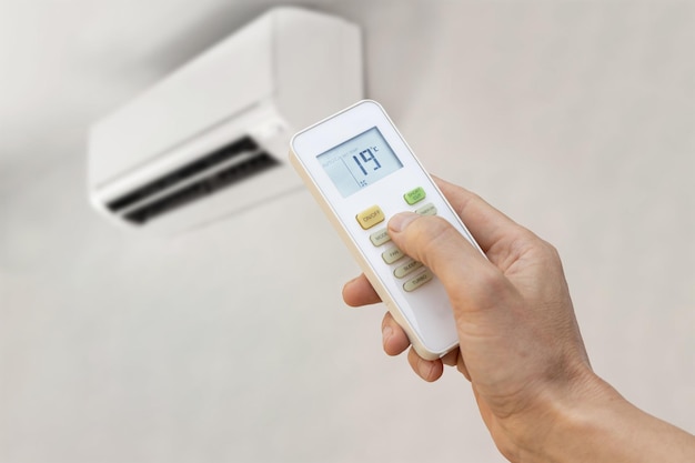 Hand with remote control of an air conditioner setting the temperature to 19 degrees Energy saving concept