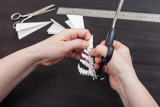 Photo hand with scissors cut snowflake from paper