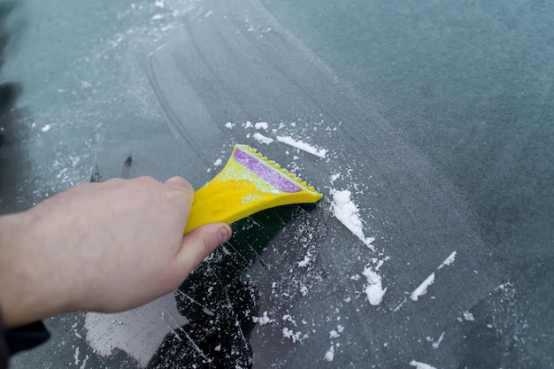 Hand with a scraper cleans the frozen car window