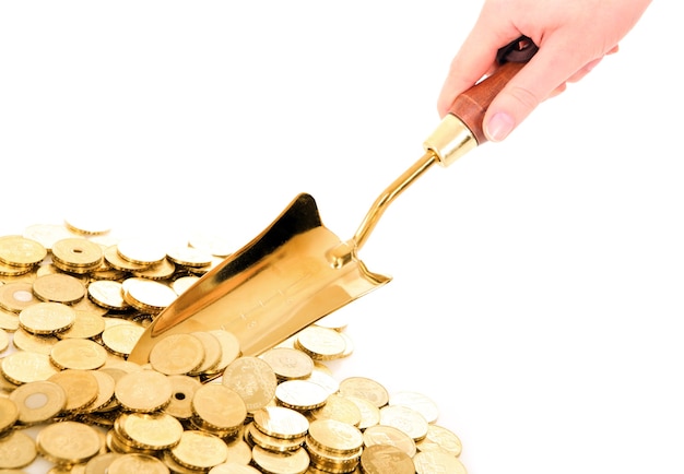 a hand with small shovel taking golden coins from a pile over white