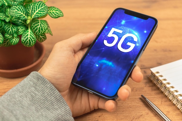 Рука со смартфоном и беспроводным подключением к сети 5G. Деловой деревянный стол фон фото