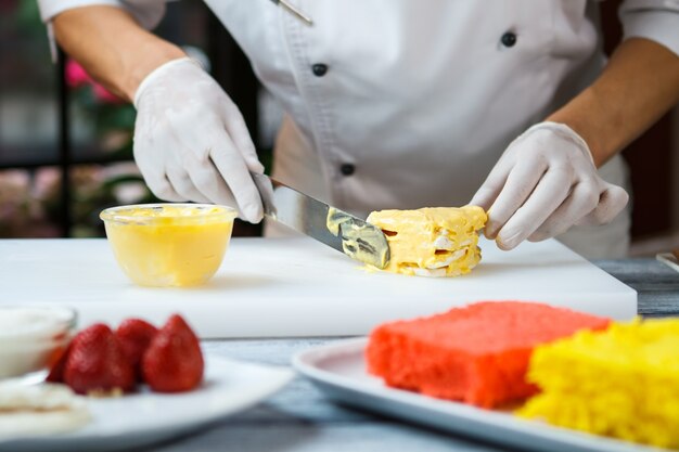 Hand with spatula touches shortcake. Shortcake smeared with custard. Chef prepares tasty dessert. Work in restaurant kitchen.