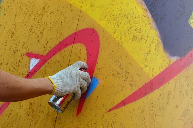 A hand with a spray can that draws a new graffiti on the wall. 