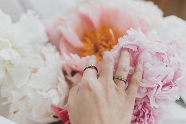 Hand with stylish rings on beautiful peonies bouquet Tender image Feminine essentials