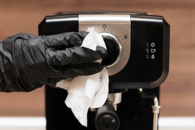 Foto mano con guanto chirurgico che disinfetta la macchina per caffè espresso
