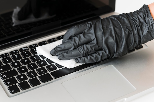 Photo hand with surgical glove disinfecting laptop surface