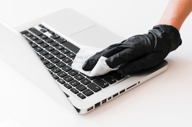 Hand with surgical glove disinfecting laptop