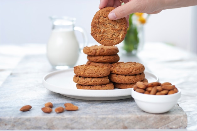 Hand with tasty oatmeal almond cookies with jar of milk on old marble table