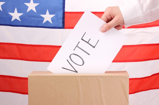 Hand with voting ballot and box on Flag of USA