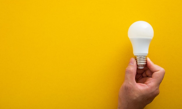 Hand with white light bulb on bright yellow background in pastel colors bright idea concept