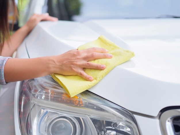 Hand with yellow microfiber cloth cleaning white car.