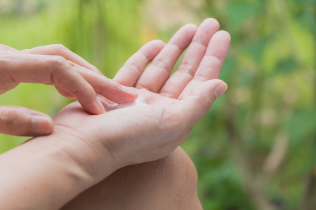 hand of woman apply lotion on skin of hand on nature table.