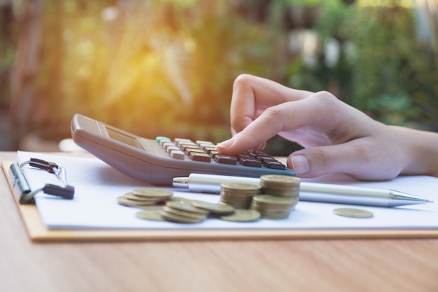 Hand of woman are pressing the calculator with stack coins on the table.