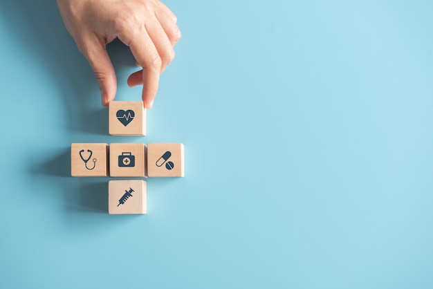 Mano della donna che sistema il cubo di legno che impila con l'assistenza sanitaria dell'icona medica sul blu