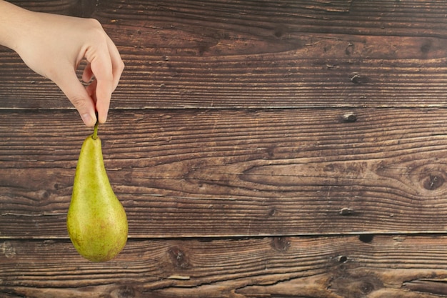 Photo hand of woman holding delicious ripe pear over a wooden wall.