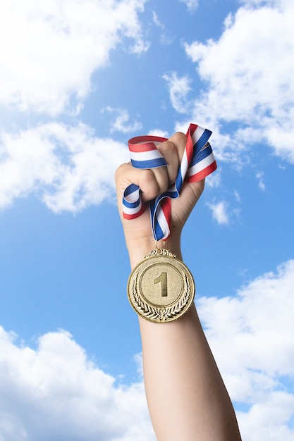 Photo hand of woman holding gold medal against sky.award and victory concept.copy space