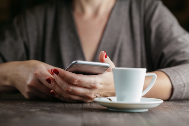 Telefono e tazza di caffè della tenuta della donna della mano