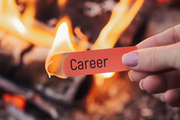 Hand of a woman holding red small sheet of paper with word career on it with bonfire on background Symbol of burning hopes on success in professional life