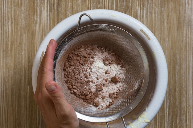 Hand of woman holding sifter with flour cocoa powder during the sifting