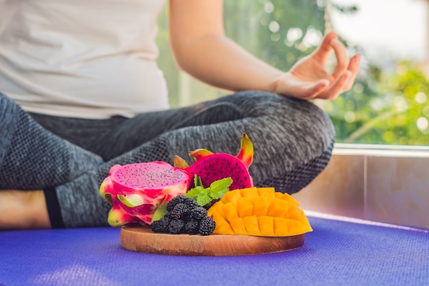 Hand of woman meditating in front of dish with dragon fruit, mango and mulberry