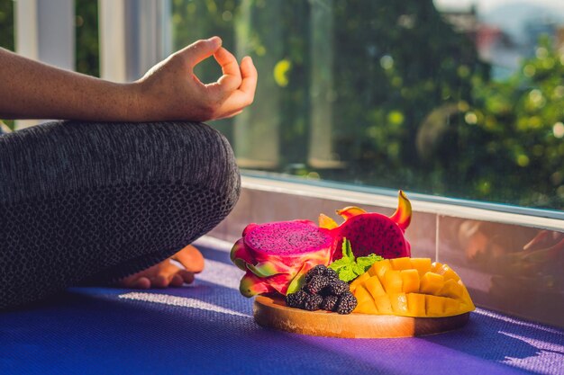 Hand of a woman meditating in a yoga pose sitting in lotus with fruits in front of her dragon fruit