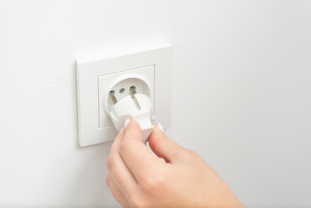 Hand of a woman plugging in an electric cord into a white european socket