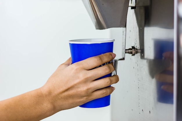 hand of woman serving ice of  ice maker machine in plastic cup