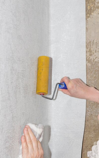 Hand of a woman smoothes air and glue bubbles on the wallpaper with a roller