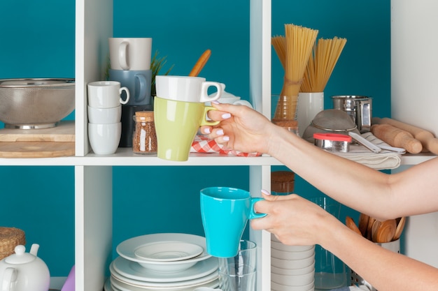 Hand of a woman taking kitchenware from a kitchen shelf