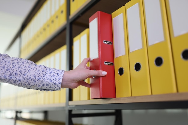 Hand of woman taking red ring binder with accounting papers from office archive organized