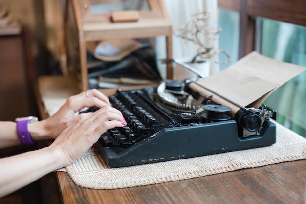 Hand of woman typing on old vintage typewriter with paper