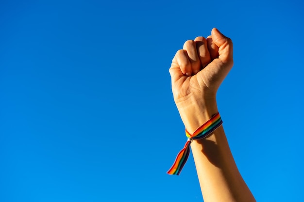 Рука женщины со сжатым кулаком в пользу феминизма на фоне голубого неба, борющегося в пользу женщин Женская сила Флаг ЛГТБ