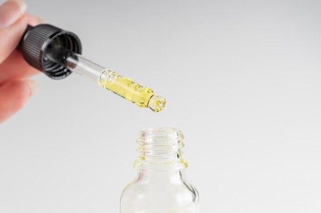 hand of woman with pipette drop of serum with retinol on gray background skin care treatment for aged skin