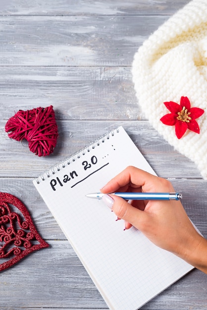 Hand of woman writing on notepad Christmas greetings with decoration on wooden 