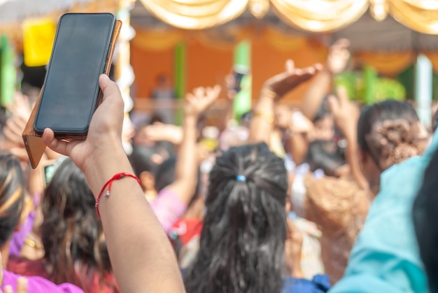 スマートフォンを持った女性が携帯電話を撮影し、民族衣装を着たビルマ人がカティン祭りに参加して踊りに来ます