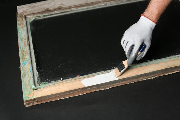 Photo hand of worker painting frame of old window on dark background